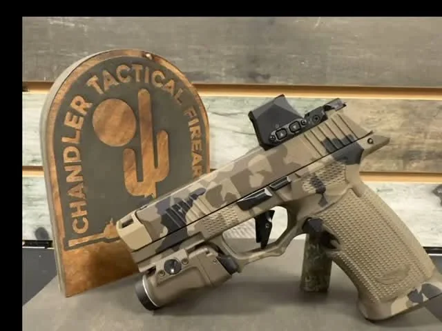 A camouflage-finished pistol with a mounted optic and weapon light.