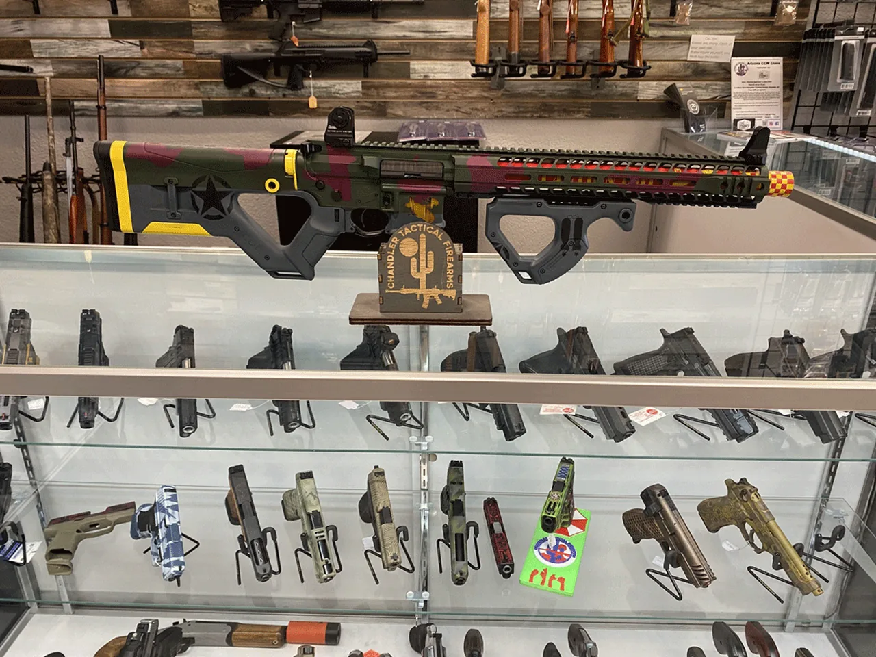 A finished long gun above a display of handgun slides in varied colors and patterns.